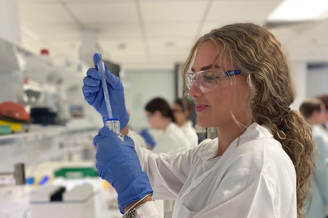 Female student in research lab wearing science glasses and lab coat.